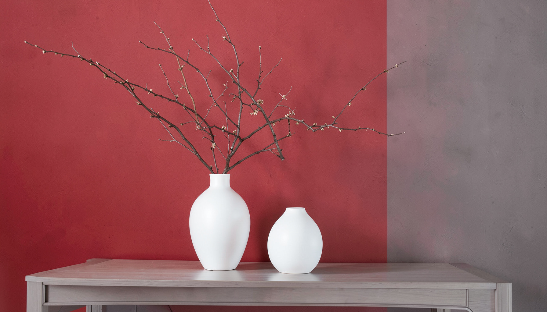 Elegant interior arrangement with white vases and decorative branch against a red-gray wall, suggesting creative and event services.
