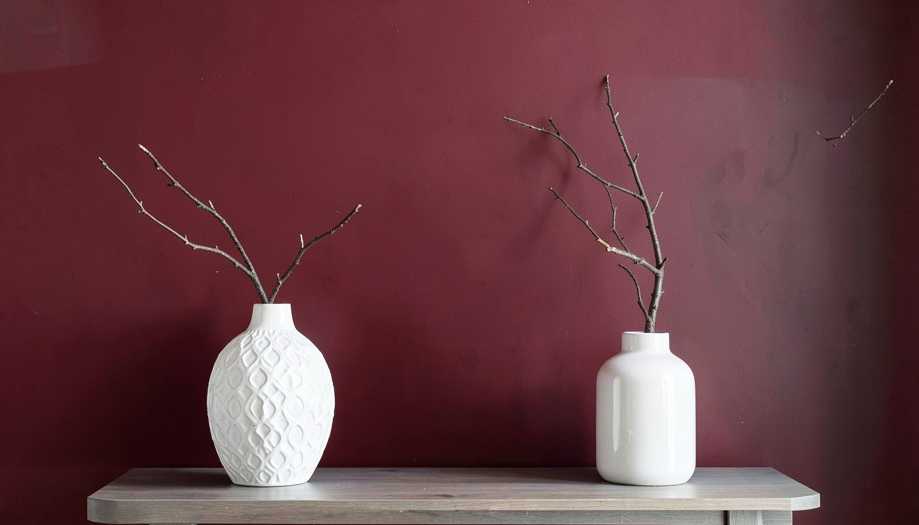 Stylish interior wall in deep red and gray tones with decorative white vases and a branch, evoking creative home decor and design services.